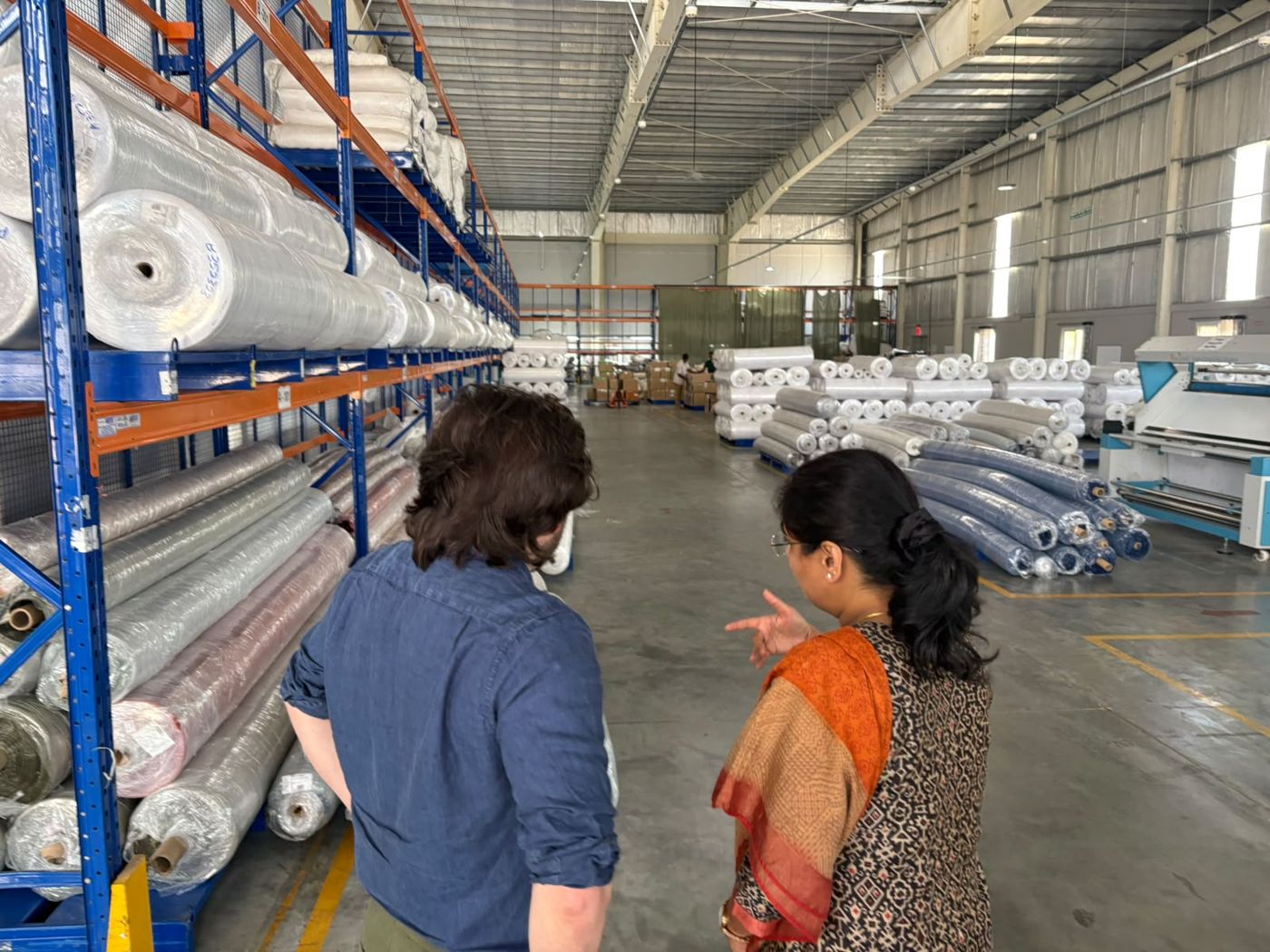 Rhys being walked through a textile warehouse, rows of fabric rolls on racking either side